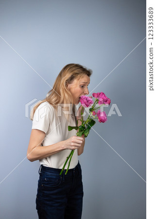 on light gray background a young blonde girl in a light T-shirt in her hands pink peony roses March 8th looks away in a state of shock marriage proposal on light gray background a young blonde girl in a light T-shirt in her hands pink peony roses March 8th looks away in a state of shock marriage proposal 123333689