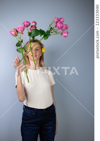 on light gray background a young blonde girl in a light T-shirt throws pink peony roses in front of her March 8 yellow flowers for separation smile on her face on light gray background a young blonde girl in a light T-shirt throws pink peony roses in front of her March 8 yellow flowers for separation smile on her face 123333690