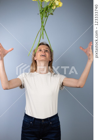 on light gray background a young blonde girl in a light T-shirt throws peony roses in front of her March 8 yellow flowers for separation smile on her face 123333740