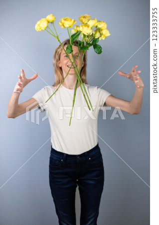 on light gray background a young blonde girl in a light T-shirt throws peony roses in front of her March 8 yellow flowers for separation smile on her face 123333755