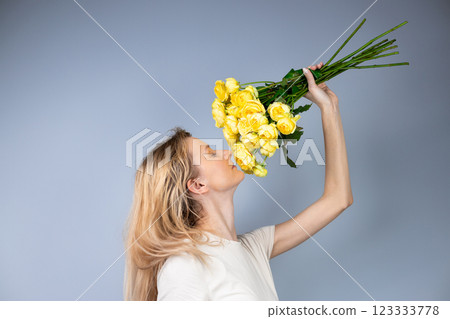 on light gray background a young blonde girl with a large bouquet of yellow peony roses women's holiday March 8 first date the girl stands with her back turned to the side sniffing flowers on light gray background a young blonde girl with a large bouquet of yellow peony roses women's holiday March 8 first date the girl stands with her back turned to the side sniffing flowers 123333778