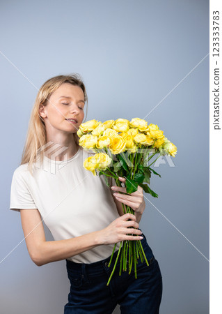 on light gray background a young blonde girl with a large bouquet of yellow peony roses women's holiday March 8 first date emotions on the face smiling girl with eyes closed on light gray background a young blonde girl with a large bouquet of yellow peony roses women's holiday March 8 first date emotions on the face smiling girl with eyes closed 123333783