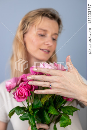closeup on light gray background a young blonde girl with a large bouquet of pink peony roses women's holiday March 8 marriage proposal emotions on the face smiling girl hand with a ring closeup on light gray background a young blonde girl with a large bouquet of pink peony roses women's holiday March 8 marriage proposal emotions on the face smiling girl hand with a ring 123333787
