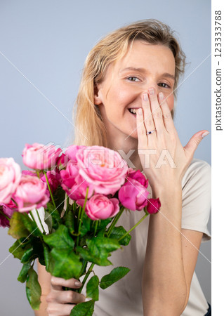 closeup on light gray background a young blonde girl with a large bouquet of pink peony roses women's holiday March 8 marriage proposal emotions on the face smiling girl hand with a ring 123333788