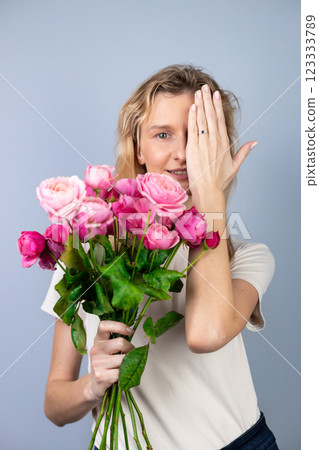 on light gray background a young blonde girl with a large bouquet of pink peony roses women's holiday March 8 marriage proposal emotions on the face smiling girl hand with a ring 123333789