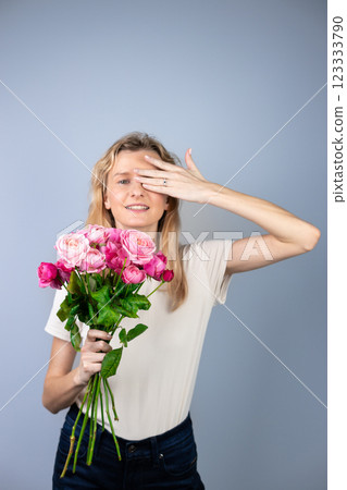 on light gray background a young blonde girl with a large bouquet of pink peony roses women's holiday March 8 marriage proposal emotions on the face smiling girl hand with a ring 123333790