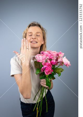 on light gray background a young blonde girl with a large bouquet of pink peony roses women's holiday March 8 marriage proposal emotions on the face smiling girl hand with a ring 123333792