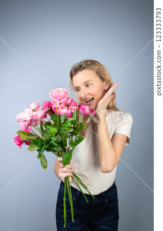 closeup gray background a young blonde girl with a large bouquet of pink peony roses women's holiday March 8 first date smiling raised palm to the side 123333793