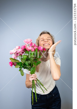 closeup gray background a young blonde girl with a large bouquet of pink peony roses women's holiday March 8 first date smiling raised palm to the side 123333794