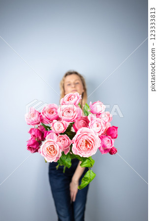 on light gray background a young blonde girl with a large bouquet of pink peony roses women's holiday the eighth of March first date emotions on the face smiling girl in the background out of focus 123333813