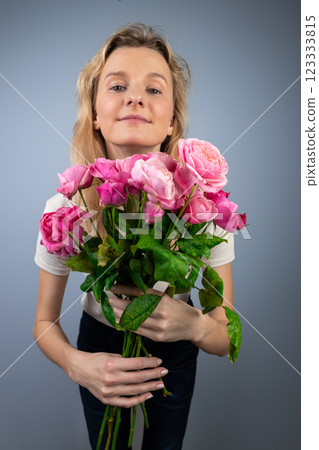 on a light gray background a young blonde girl with a large bouquet of pink peony roses women's holiday March 8 first date emotions on the face smiling girl leaning forward to the camera on a light gray background a young blonde girl with a large bouquet of pink peony roses women's holiday March 8 first date emotions on the face smiling girl leaning forward to the camera 123333815