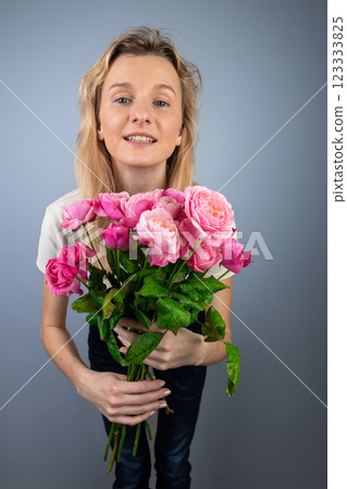 on a light gray background a young blonde girl with a large bouquet of pink peony roses women's holiday March 8 first date emotions on the face smiling girl leaning forward to the camera on a light gray background a young blonde girl with a large bouquet of pink peony roses women's holiday March 8 first date emotions on the face smiling girl leaning forward to the camera 123333825