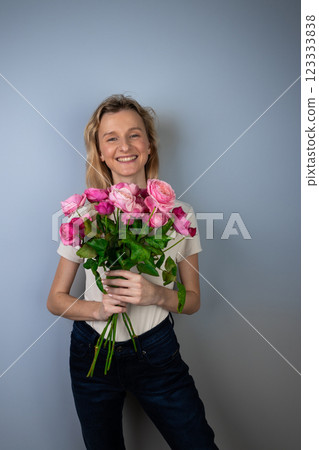 on a light gray background a young blonde girl with a large bouquet of pink peony roses women's holiday March 8 first date emotions on the face smiling girl 123333838