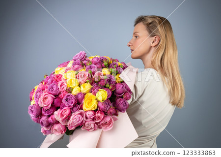 on light gray background a young blonde girl with a large bouquet of pink peony roses women's holiday March 8 first date the girl stands with her back turned to the side 123333863