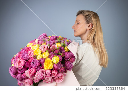 on light gray background a young blonde girl with a large bouquet of pink peony roses women's holiday March 8 first date the girl stands with her back turned to the side 123333864