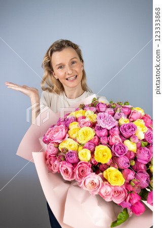 closeup gray background a young blonde girl with a large bouquet of pink peony roses women's holiday March 8 first date smiling raised palm to the side closeup gray background a young blonde girl with a large bouquet of pink peony roses women's holiday March 8 first date smiling raised palm to the side 123333868