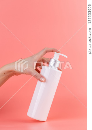 close-up on a soft pink background white glossy bottle with dispenser minimalist container for cosmetics beauty industry hermetic storage of liquids female hand presses the dispenser with a finger close-up on a soft pink background white glossy bottle with dispenser minimalist container for cosmetics beauty industry hermetic storage of liquids female hand presses the dispenser with a finger 123333906