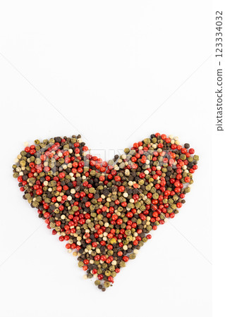 closeup white background a pile of mixed large aromatic peppers black red and white the main seasoning for food peppercorns indian and european spices pepper laid out in the shape of a heart 123334032