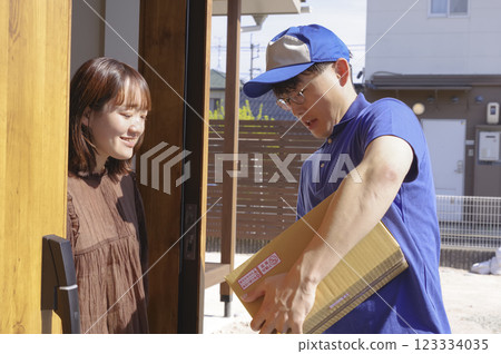 A woman and a delivery staff member receiving a package at the front door A woman and a delivery staff member receiving a package at the front door 123334035