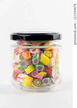 on white background in a small transparent jar multi-colored sugar caramels with different flavors and patterns children's favorite sweets large selection risk of caries blood sugar excess weight 123334076