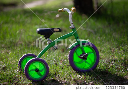 A green tricycle with purple wheels sits on the grass. The tricycle is old and has a vintage look to it A green tricycle with purple wheels sits on the grass. The tricycle is old and has a vintage look to it 123334760