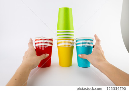 white background stack of paper cups for coffee and tea painted in red green yellow and blue colors disposable tableware attributes for trips recreation and picnics eco-cups woman hands take them 123334790