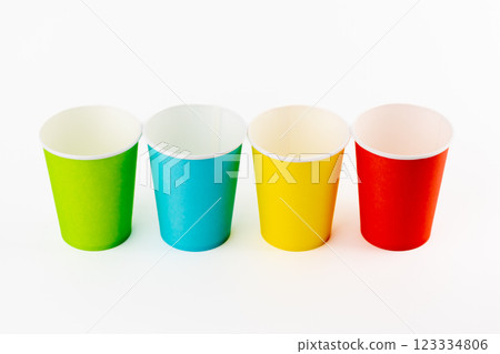 top shot white background, four paper cups for coffee and tea painted in red, green, yellow and blue, disposable tableware, attributes for trips, recreation and picnics, eco cups, waterproof 123334806