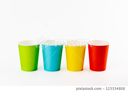 on white background, four paper cups for coffee and tea painted in red, green, yellow and blue, disposable tableware, attributes for trips, recreation and picnics, eco cups, waterproof 123334808