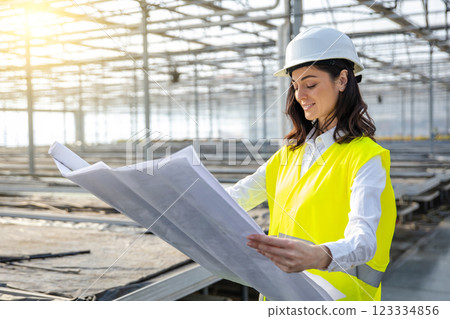 Female engineer in a greenhouse construction site scrutinizing a sketch 123334856