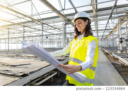 Female engineer in a greenhouse construction site scrutinizing a sketch 123334864