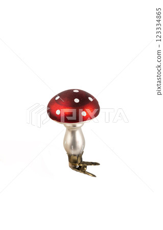 closeup on white background in the air, a glass enameled Christmas tree toy in the shape of a fly mushroom with a clip at the base, a modern decor toy with sparkles 123334865