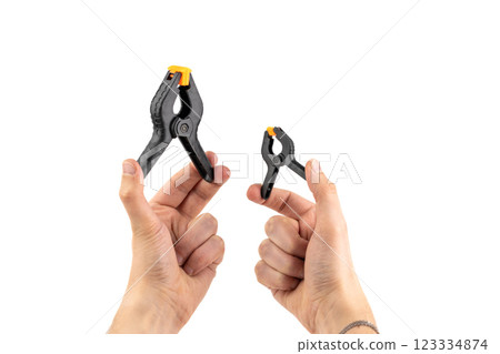 on white background, two male hands hold a large and a small plastic black clamp with an orange lock, a tool in everyday life, a reliable fixation, a repair tool on white background, two male hands hold a large and a small plastic black clamp with an orange lock, a tool in everyday life, a reliable fixation, a repair tool 123334874
