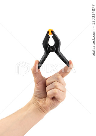 close-up on white background, a man's hand holds a large plastic black clamp with an orange lock, a tool in everyday life, a reliable fixation, a repair tool close-up on white background, a man's hand holds a large plastic black clamp with an orange lock, a tool in everyday life, a reliable fixation, a repair tool 123334877