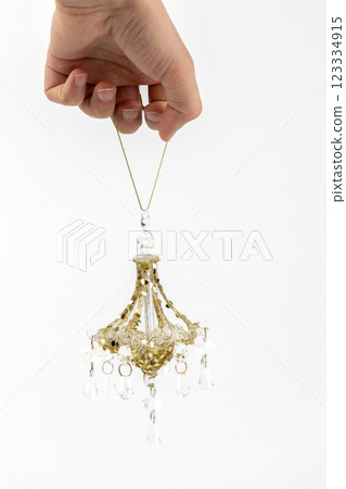 closeup on white background a man's hand holds a glass enameled Christmas tree toy in the shape of an old crystal chandelier modern decor toy with sparkles closeup on white background a man's hand holds a glass enameled Christmas tree toy in the shape of an old crystal chandelier modern decor toy with sparkles 123334915