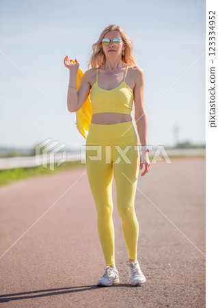 A middle-aged woman in a yellow sports outfit walks along the road. 123334952
