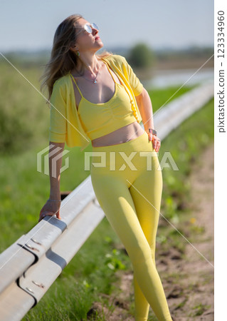 A beautiful adult woman in yellow sportswear is resting after jogging. 123334960