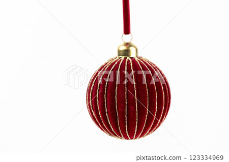 close up on white background suspended red round velvet Christmas tree toy with gold piping on a red rope New Year's toys modern decor toys with sparkles 123334969