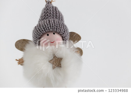 close-up of hanging textile soft Christmas tree toy in the form of a fluffy round angel in a gray hat, pastel colors, modern decor, legs on strings close-up of hanging textile soft Christmas tree toy in the form of a fluffy round angel in a gray hat, pastel colors, modern decor, legs on strings 123334988