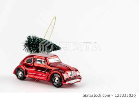 on white background there is a glass enameled Christmas tree toy in the shape of a red retro car that is carrying a Christmas tree, a modern decor toy with sparkles white 123335020