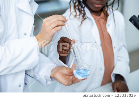 Scientists examining liquid in conical flask conducting test in lab investigating chemical reactions Scientists examining liquid in conical flask conducting test in lab investigating chemical reactions 123335029
