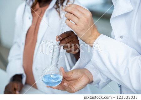 Diverse scientists' hands with flask that has blue chemical liquid making tests in laboratory Diverse scientists' hands with flask that has blue chemical liquid making tests in laboratory 123335033