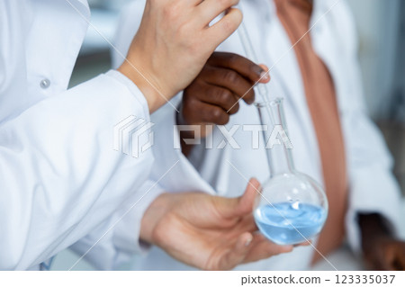 Diverse medical woman and man in laboratory holding transparent flask with chemical solution Diverse medical woman and man in laboratory holding transparent flask with chemical solution 123335037