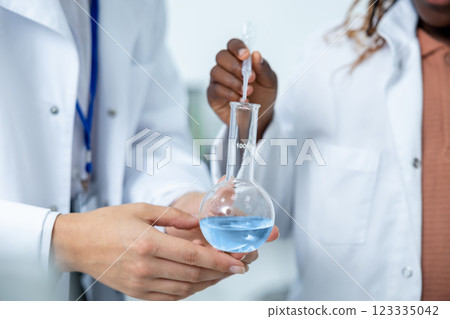 Diverse scientists' hands with flask that has blue chemical liquid making tests in laboratory 123335042