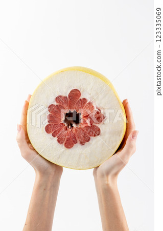 closeup on white photo background, thin female hands hold a large pamella fruit, cut in half, a little pulp, thick skin, tropical yellow fruit, healthy vitamins, seasonal fruit, vitamin C closeup on white photo background, thin female hands hold a large pamella fruit, cut in half, a little pulp, thick skin, tropical yellow fruit, healthy vitamins, seasonal fruit, vitamin C 123335069