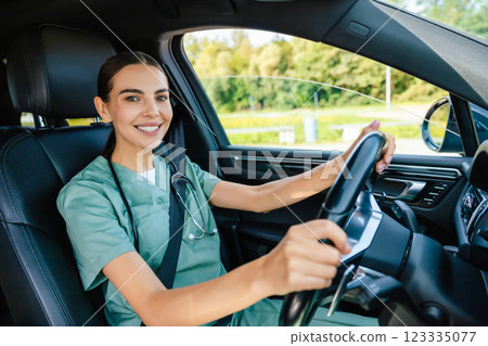 Smiling beaming young woman in scrub suit driving a car 123335077
