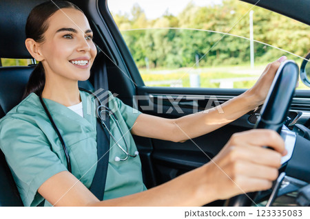 Smiling beaming young woman in scrub suit driving a car 123335083