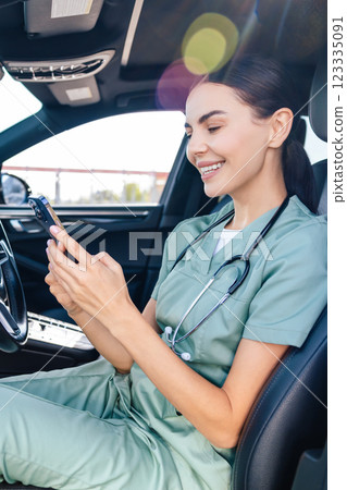 Smiling pretty female doctor sitting in a car and talking on the phone Smiling pretty female doctor sitting in a car and talking on the phone 123335091