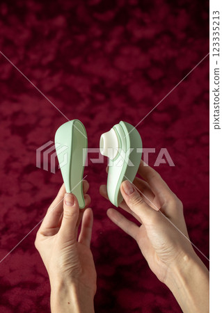 on red burgundy velvet background, female hands, a vacuum vibrator and its cover, gently mint color, a device for girls, relaxation for adults, egg shape, magnetic charging, water resistance 123335213