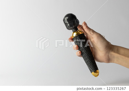 white background woman's hand with lubricant on her fingers holds a black large vibrator in the shape of a microphone doused with transparent water lubricant sexual pleasure toys for adults 123335267