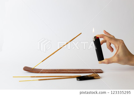 close-up on white background on a long brown stand with stars for incense sticks a new beige palosanto meditation stick is placed a hand with a black lighter setting fire close-up on white background on a long brown stand with stars for incense sticks a new beige palosanto meditation stick is placed a hand with a black lighter setting fire 123335295
